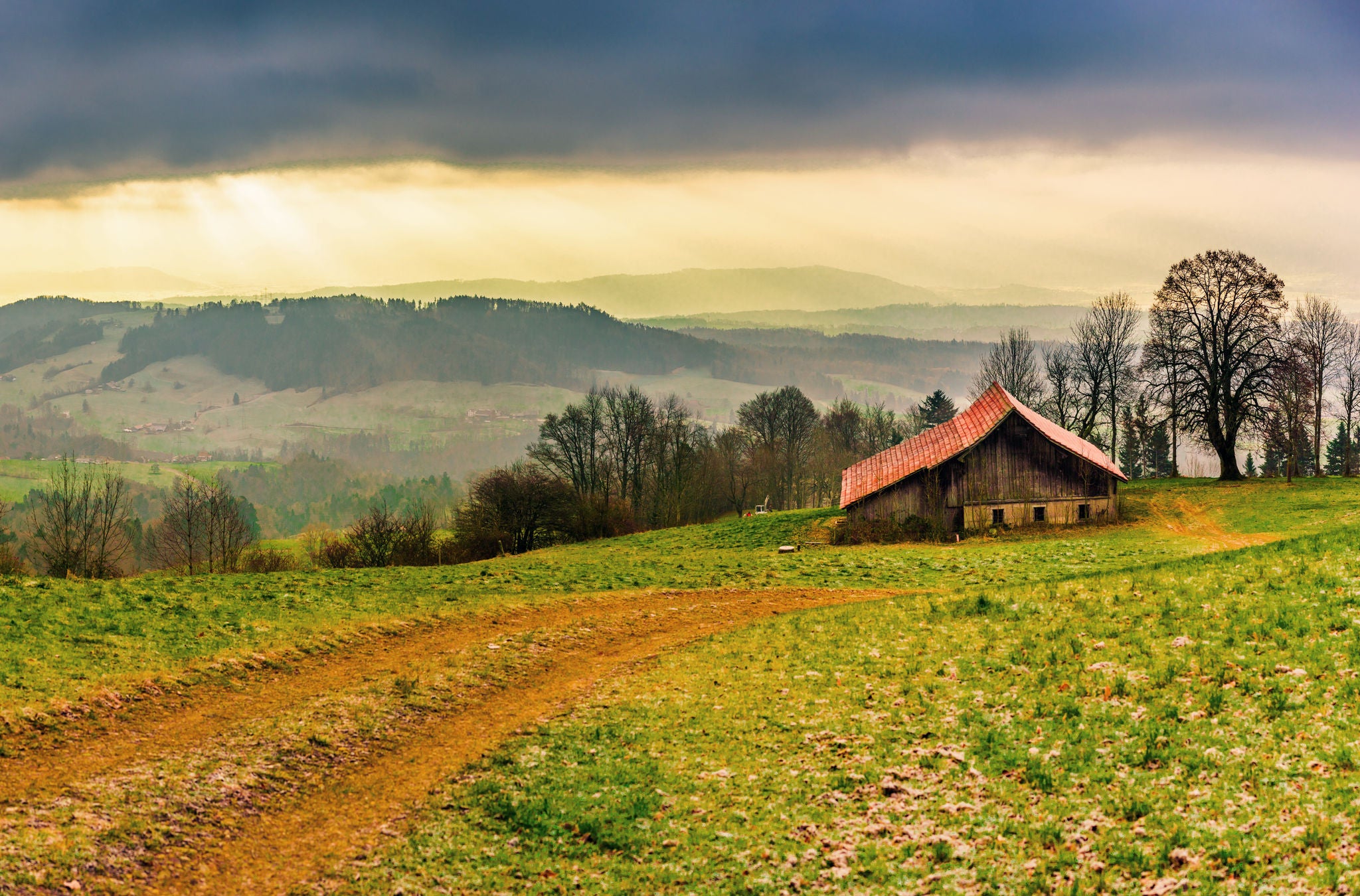 Eine Scheune steht auf der Wiese, hinten erscheint eine Regenwolke in der abendlichen Stimmung. 