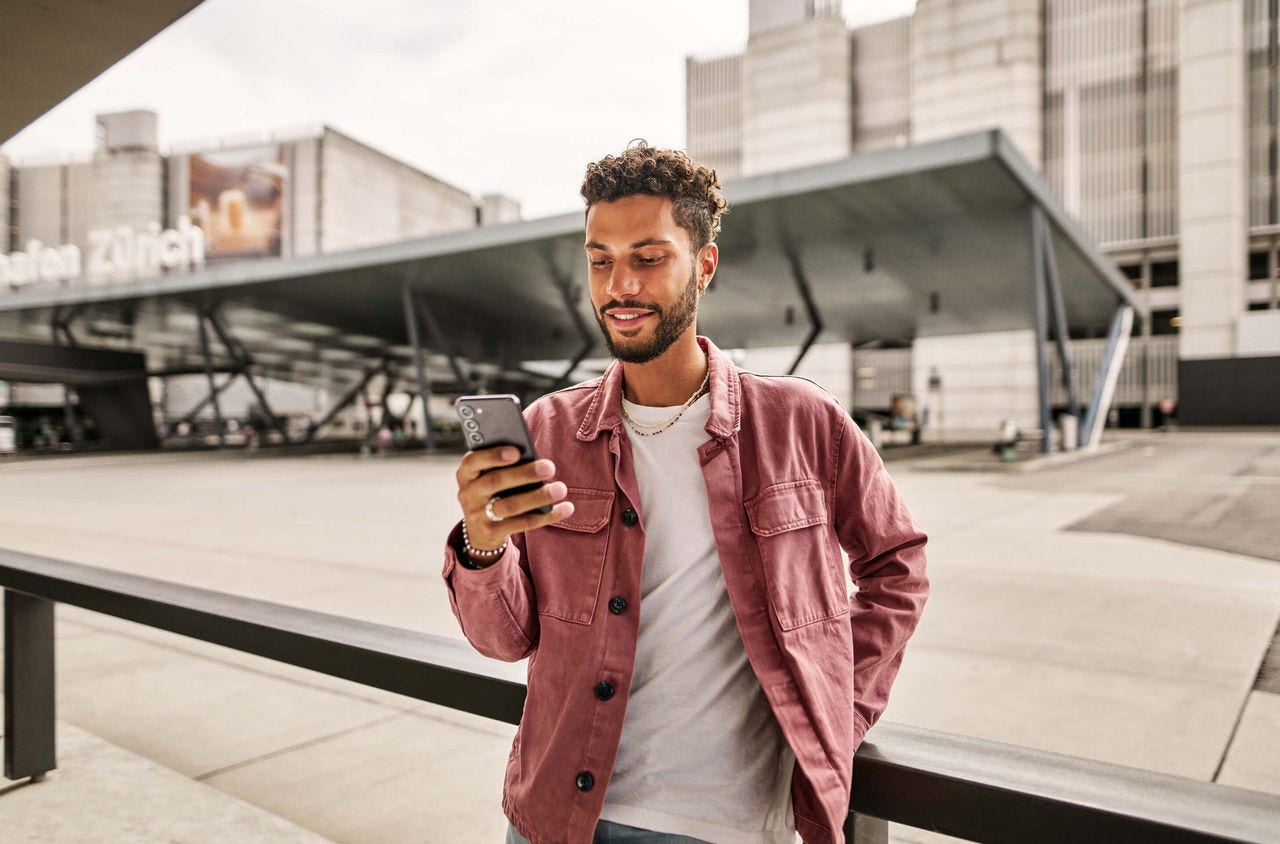 Immer informiert mit der ZVV-App Ein junger Mann an der Haltestelle Zürich Flughafen prüft in der ZVV-App ob seine Verbindung pünktlich fährt.