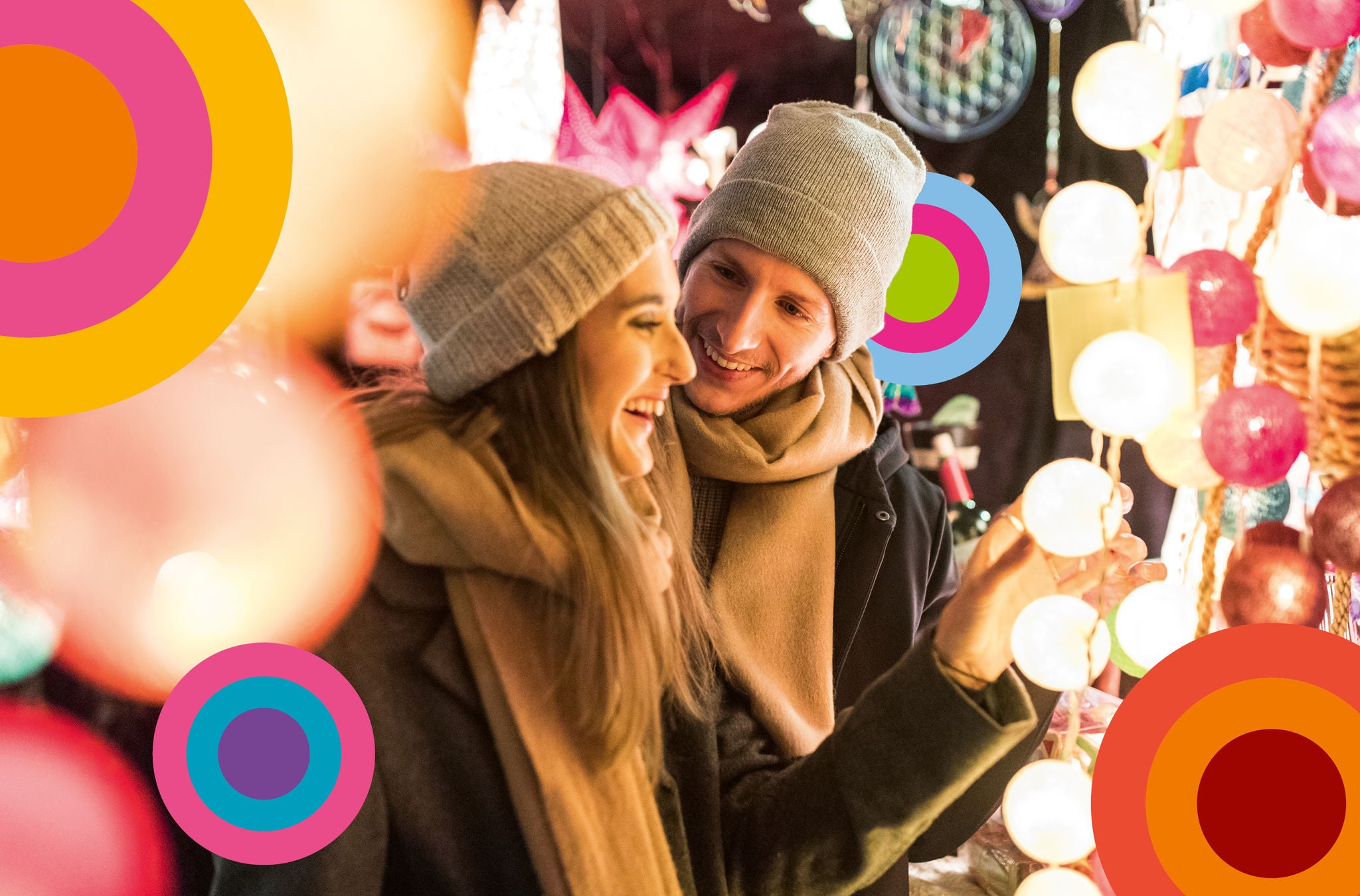 Paar am Weihnachtsmarkt umgeben von Lichterketten.