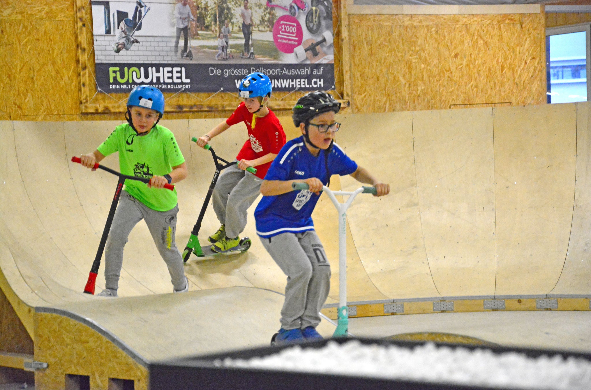 Drei Kinder mit dem Scooter auf der Rampe des Geisterkickboarder Skatepark in Wetzikon.