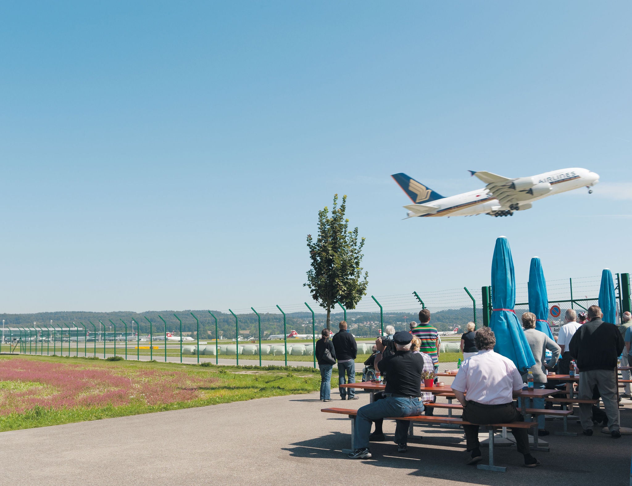 Flugzeug hebt gerade ab und Zuschauer beobachten es vor dem Zaun