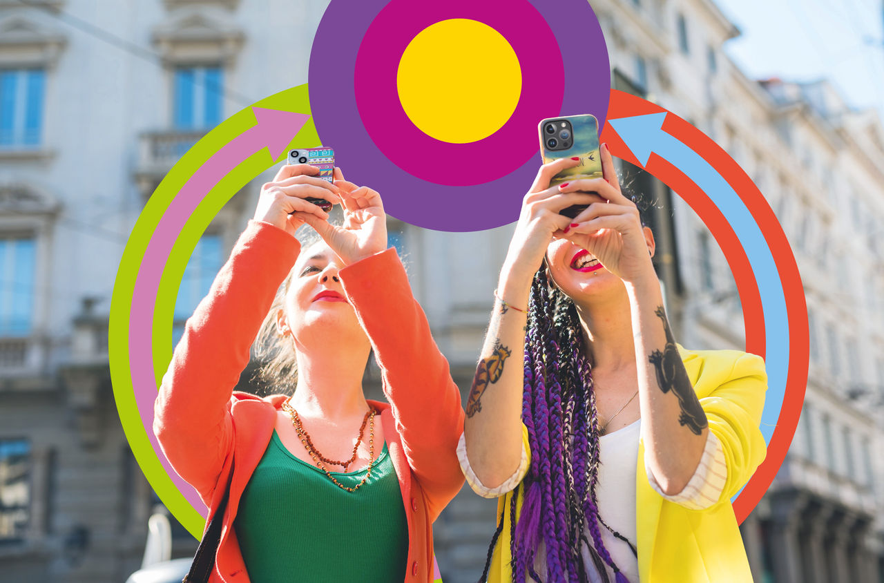 Freundinnen am Fotografieren mit ZVV-Grafikelementen Zwei Freundinnen machen mit ihren Smartphones Fotos in einer urbanen Umgebung. Im Hintergrund sind farbige ZVV-Grafikelemente.